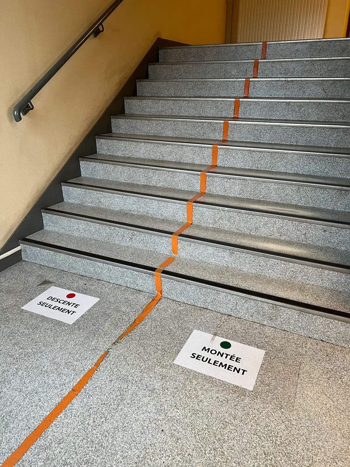 A stairwell split down the middle with orange tape, with floor signs reading DESCENTE SEULEMENT on one side and MONTÉE SEULEMENT on the other