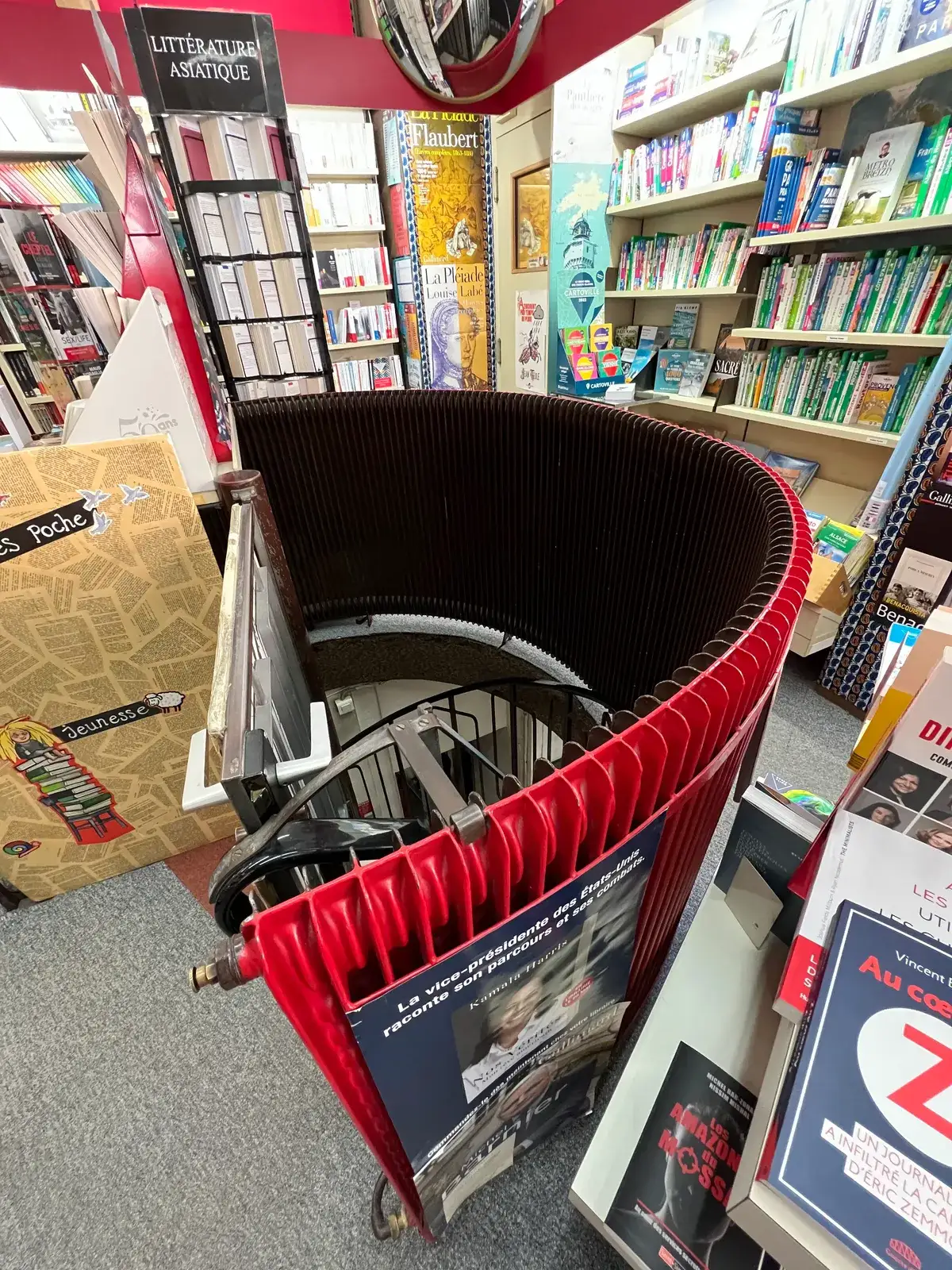 A curved red and black radiator curling around the top of a spiral staircase in a bookshop, doubling as a barrier