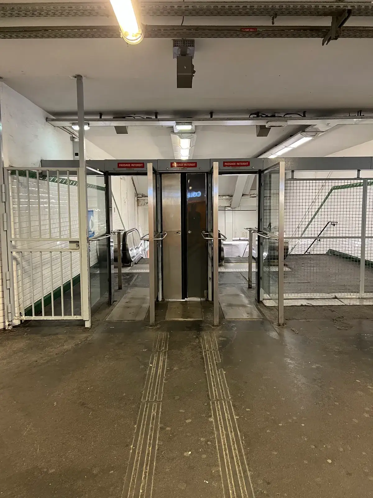 A bank of metro exit gates labeled PASSAGE INTERDIT, with the side gate standing wide open
